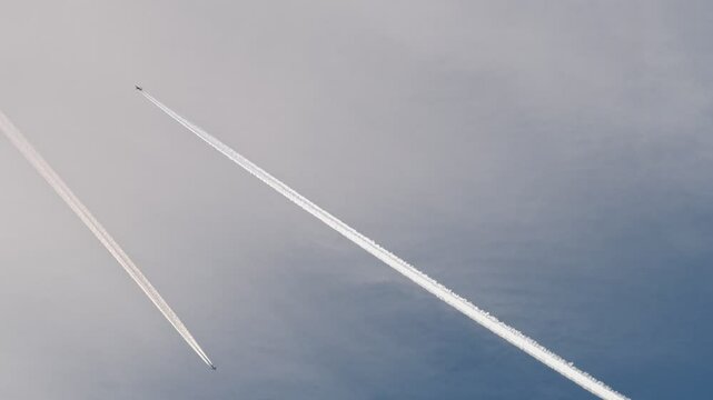 Two airplanes are crossing paths in the sky, leaving behind visible contrails that trace their flight paths
