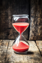 hourglass with red sand on a rustic wooden surface