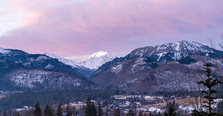 Winter landscape of mountain peaks and valley with houses at sunrise.