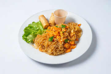 thai soya noodles with vegetables and fried spring rolls on a plate isolated on a white background traditional Thai dish.