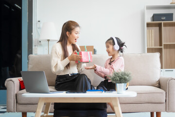 Asian young mother and her daughter sit together on the sofa in the cozy living room, working on homework at the desk, creating a warm and supportive atmosphere for learning, love, hug, mother days.