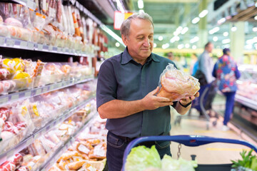 Mature man choosing packaged piece of meat in grocery store