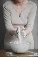 a woman kneads dough with flour in her hands over a transparent bowl