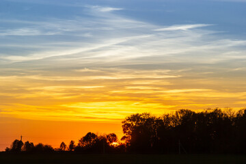 Vibrant sunset over a tranquil landscape with trees silhouetted against the colorful sky in a rural setting