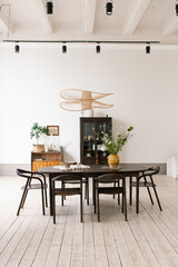 Large oval wooden table with chandelier hanging above it. Vase of flowers and potted plant