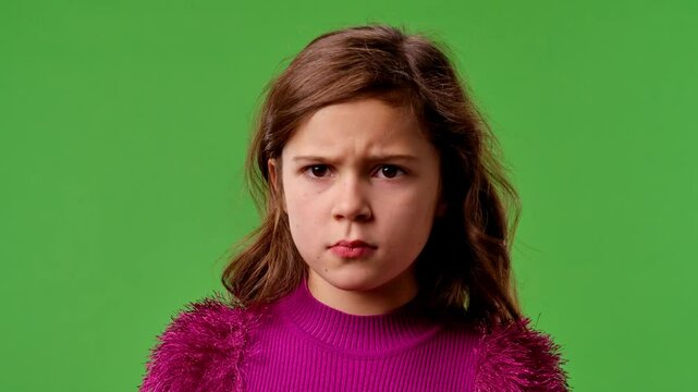 Little girl child with crossed arms and angry face stumping leg and looks at camera, negative expression, isolated on chroma key green screen studio background mockup.