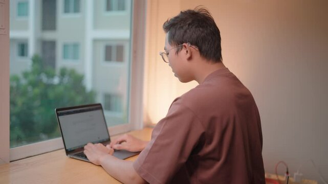 Focused Work A young man concentrates intently as he types on his laptop,  eyes fixed on the screen. The natural light streaming through the window creates a calm and focused atmosphere.