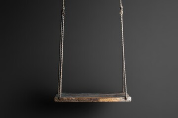 Wooden swing hangs from two ropes against a dark background