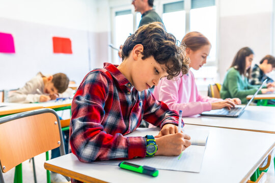 Elementary school students studying in classroom, concentrated pupils writing and using laptop