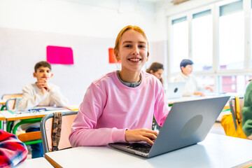 Smiling student using laptop in classroom with classmates