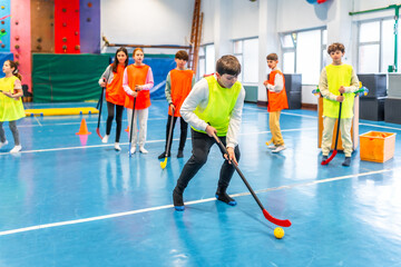 Students playing floor hockey in school gym class wearing vests