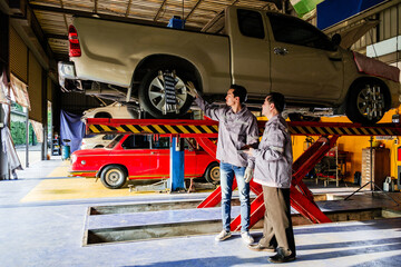 Asian mechanics inspecting a pickup truck on hydraulic lift at auto repair shop. Ideal for concepts...