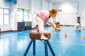 Fotobehang Gymnastiek Young girl balancing on pommel horse during gymnastics class at school gym  © unai