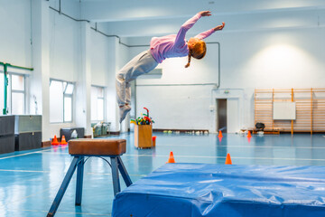 Young gymnast performing a backflip over vaulting horse in school gym