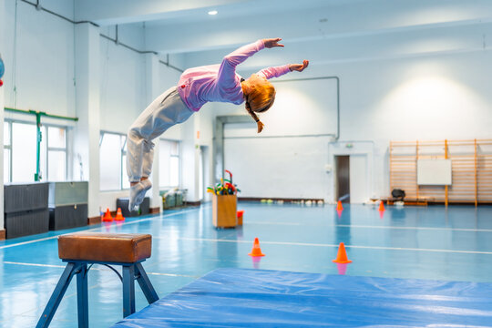 Young gymnast performing backflip over vault in school gym class