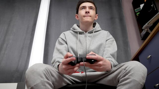 Teenager plays video games quickly pressing buttons on controller. Adolescent boy rapidly taps buttons on game controller while playing. Young male intensively presses controller buttons during video