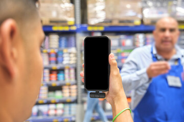 Hand holding smartphone with blank screen in warehouse with a blurred employee in background