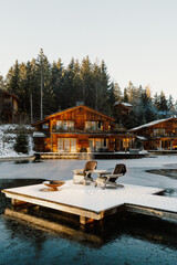 Fototapeta premium A cozy lakeside retreat at golden hour. Rustic wooden cabins, a crackling fire pit, and Adirondack chairs invite relaxation by the still water. A serene escape into nature’s beauty in Dolomites, Italy