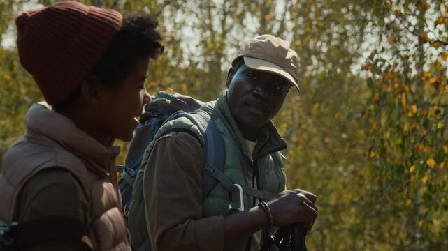 Rack focus shot of dad and son dressed in hiking clothes talking to each other and looking at surroundings during family getaway in early fall