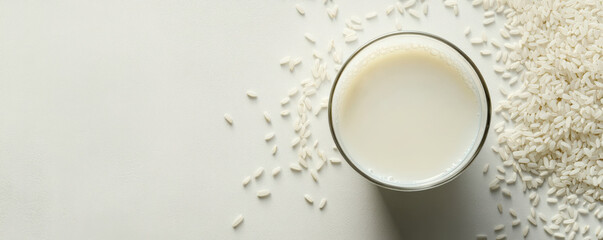 Creamy rice milk in glass beside scattered rice grains on light surface, showcasing healthy and dairy free alternative