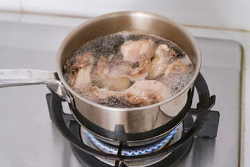 Boiled chicken in oily chicken stock in a steel saucepan on a stove
