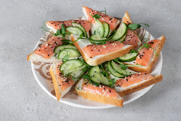 Sandwiches with salted salmon and cucumber on gray background