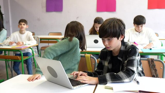 Young students work together on a laptop, demonstrating teamwork and digital literacy in a modern classroom setting