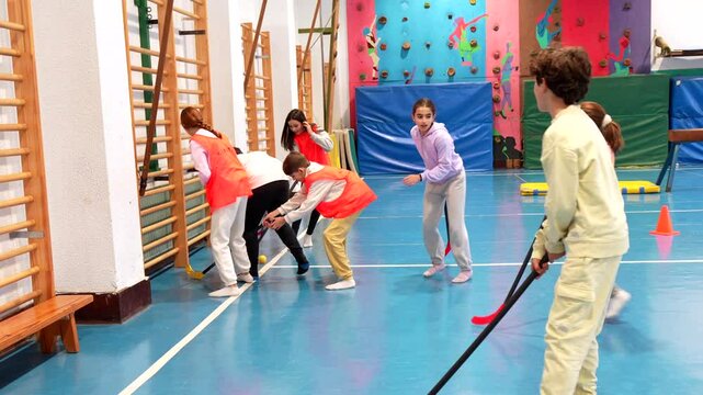 Elementary school students wearing orange and purple shirts are playing floorball in gym class