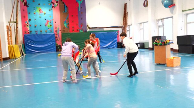Elementary school students learning and playing floorball together in gym class, promoting teamwork, coordination, and physical activity
