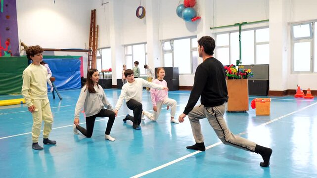Group of pre adolescent students practicing lunges with their teacher during gym class in a school gymnasium