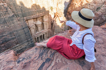 Woman traveler sitting on carpet viewpoint in Petra ancient city looking at the Treasury or...