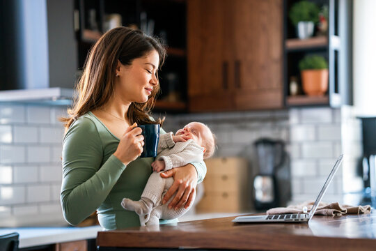 Stay at home mom working remotely on laptop while taking care of her baby. Global work on computer