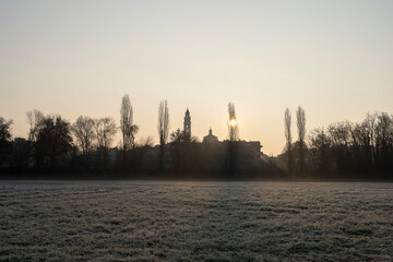 Winter morning with silhouette.
Winter morning at sunrise, frost on the grass and bell tower, church and buildings in silhouette.