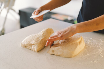 Hands are skillfully rolling and shaping dough on a clean kitchen countertop sprinkled with flour, healthy sourdough bread. The bright space suggests a cozy baking atmosphere.
