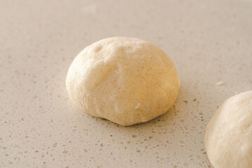 Hands are skillfully rolling and shaping dough on a clean kitchen countertop sprinkled with flour, healthy sourdough bread. The bright space suggests a cozy baking atmosphere.