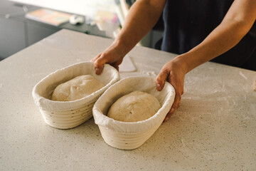 Hands are skillfully rolling and shaping dough on a clean kitchen countertop sprinkled with flour, healthy sourdough bread. The bright space suggests a cozy baking atmosphere.