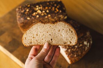 Sourdough bread, freshly baked and still warm, are stacked on a wooden surface. The bread are...
