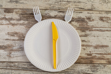 A white paper plate is placed in the center of the table, with a yellow disposable knife resembling a clock hand. The photograph symbolizes the concept of meal timing, fast food, and portioned eating.