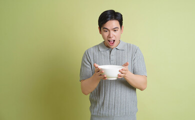 Young Asian man holding a bowl on green background