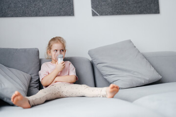 Portrait of a blond child doing inhalation on a gray sofa in the interior of the room. Lung health in children.