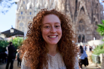 Close-up of happy young woman with curly red hair smiling looking at camera.