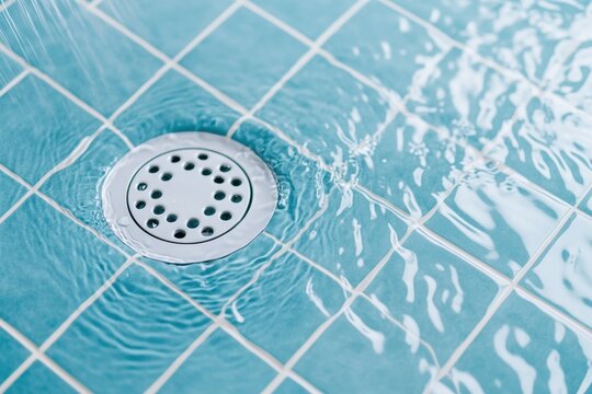 Water flows into a white circular drain on a light blue tiled shower floor, creating ripples on the surface.