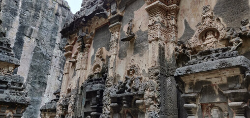 The wall is made of stone and has a lot of carvings on it. Kailasa Temple, Ellora Caves, India