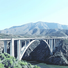 Obraz premium Mountain highway bridge spans scenic valley, blue sky background; travel, infrastructure, transportation