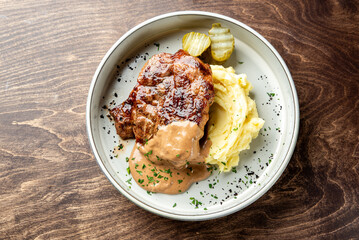 A hearty plate featuring a succulent pork chop topped with savory gravy, served alongside creamy mashed potatoes and garnished with pickles, on a rustic wooden table.
