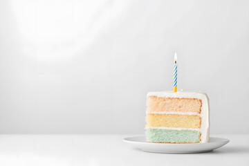 Appetizing piece of birthday cake on a plate with one burning candle isolated on white background	