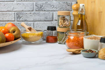 Assortment of cereals and legumes in jars, containers and bowls in the kitchen, on a light background. Free space, kitchen table, background. Healthy eating, products, vegetarianism.