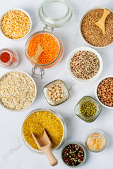 Assortment of cereals and legumes in jars, containers in bowls on a light background, top view. Healthy eating, products, vegetarianism.