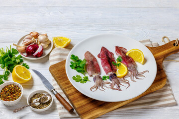 Whole fresh raw baby squid on a white plate
