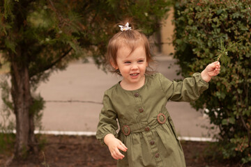 Cheerful active preschool girl in green dress playing outdoors in summer. Concept of children's fun and leisure